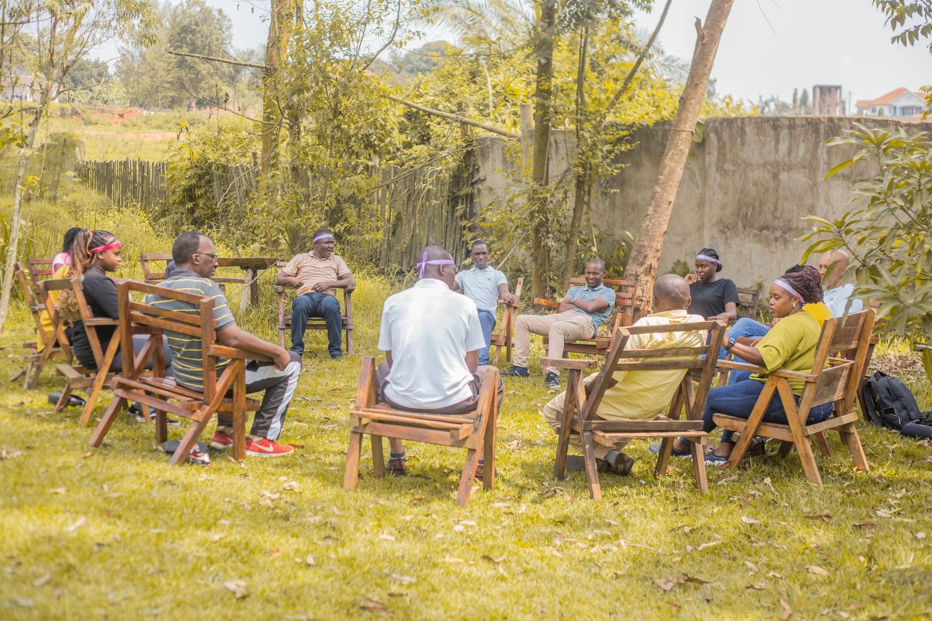 A diverse group of adults gathered outdoors for a meeting on a sunny day in a peaceful garden setting.